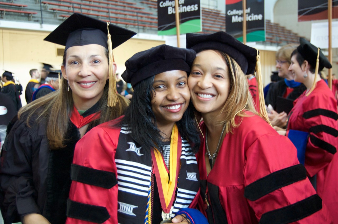 Two graduating doctoral students pose with their advisor at the hooding ceremony.